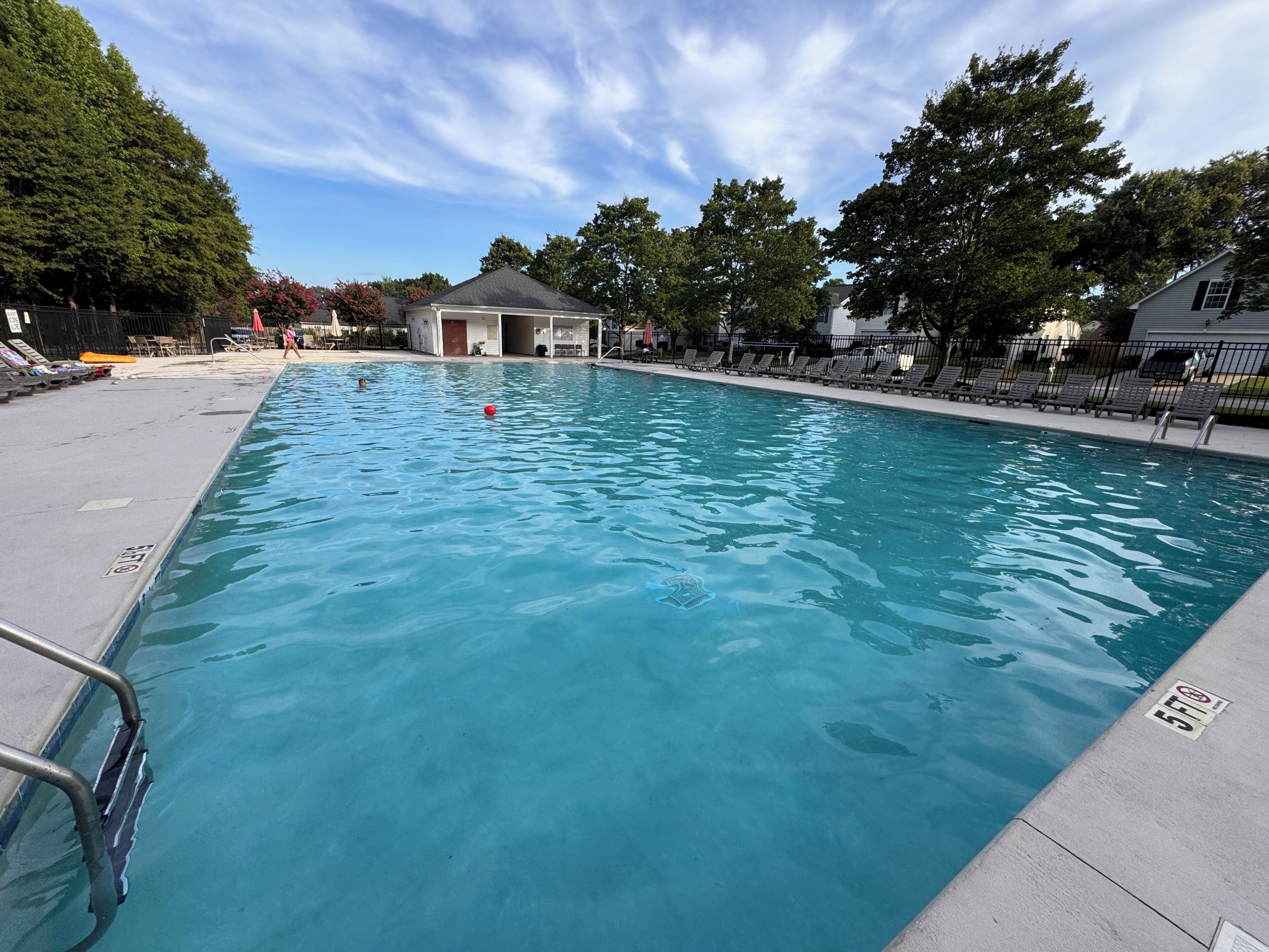 A swimming pool with a lifeguard chair, lounge chairs, and a building in the background.