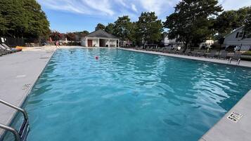 A swimming pool with a lifeguard chair, lounge chairs, and a building in the background.