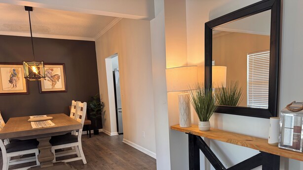 A dining area with a wooden table, chairs, a hanging light fixture, and framed artwork on the wall.