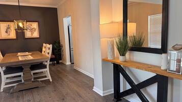 A dining area with a wooden table, chairs, a hanging light fixture, and framed artwork on the wall.
