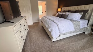 A bedroom with a bed, dresser, TV, and a door leading to another room.