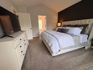 A bedroom with a bed, dresser, TV, and a door leading to another room. - HOT TUB, Community Pool, AC, 5-Bedroom Oasis in Simpsonville (Simpsonville)