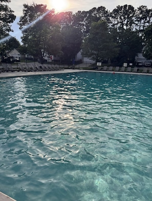 Piscina cristalina con cielo iluminado por el sol y árboles al fondo.