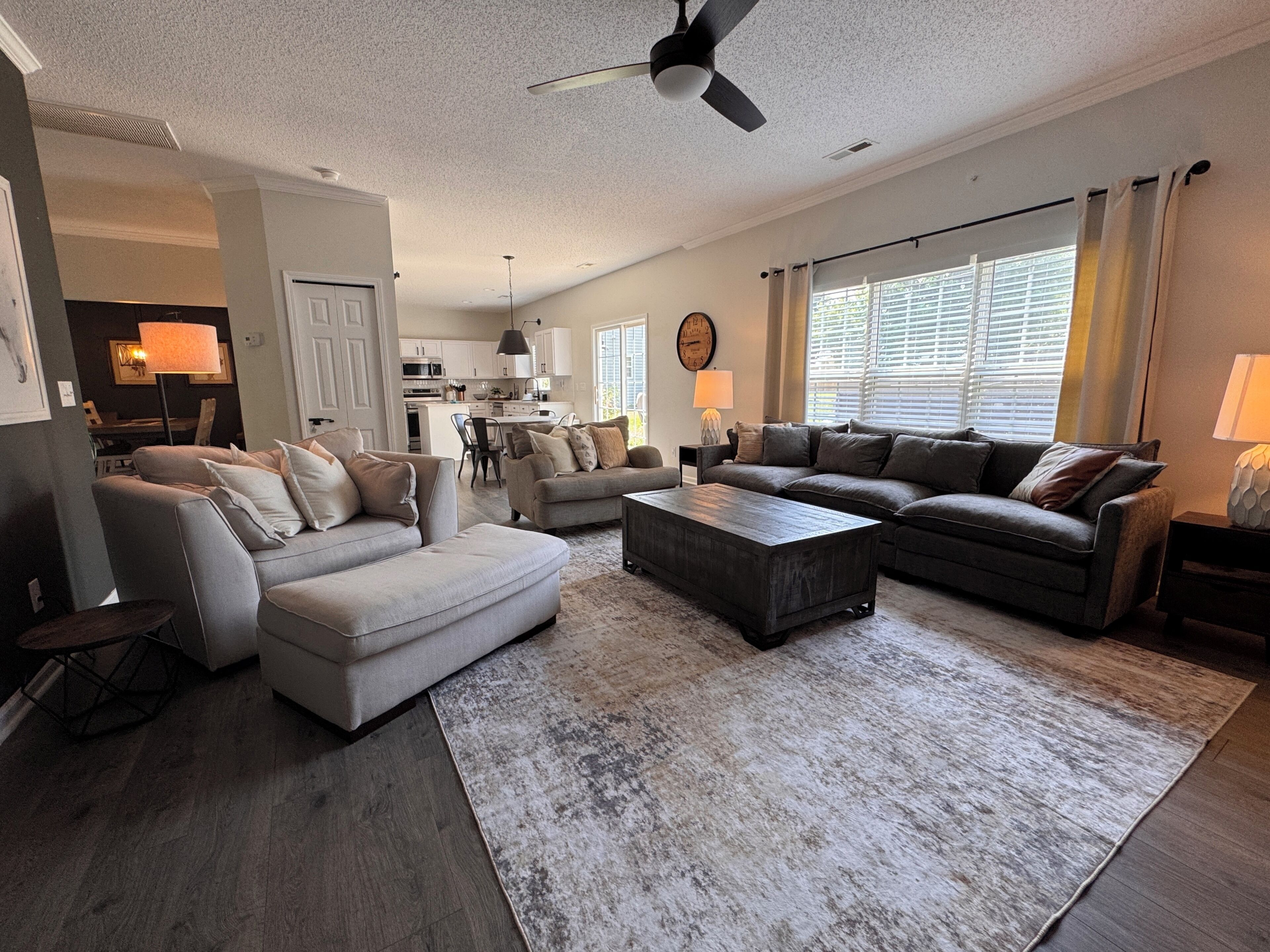 A spacious living room with a large sectional sofa, a coffee table, and a dining area with a kitchen in the background.