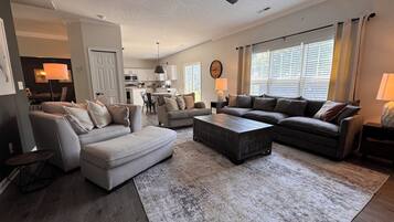 A spacious living room with a large sectional sofa, a coffee table, and a dining area with a kitchen in the background.