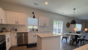 A modern kitchen with white cabinets, a dishwasher, and a dining area with a table and chairs.