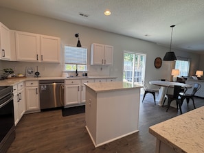 A modern kitchen with white cabinets, a dishwasher, and a dining area with a table and chairs. - HOT TUB, Community Pool, AC, 5-Bedroom Oasis in Simpsonville (Simpsonville)