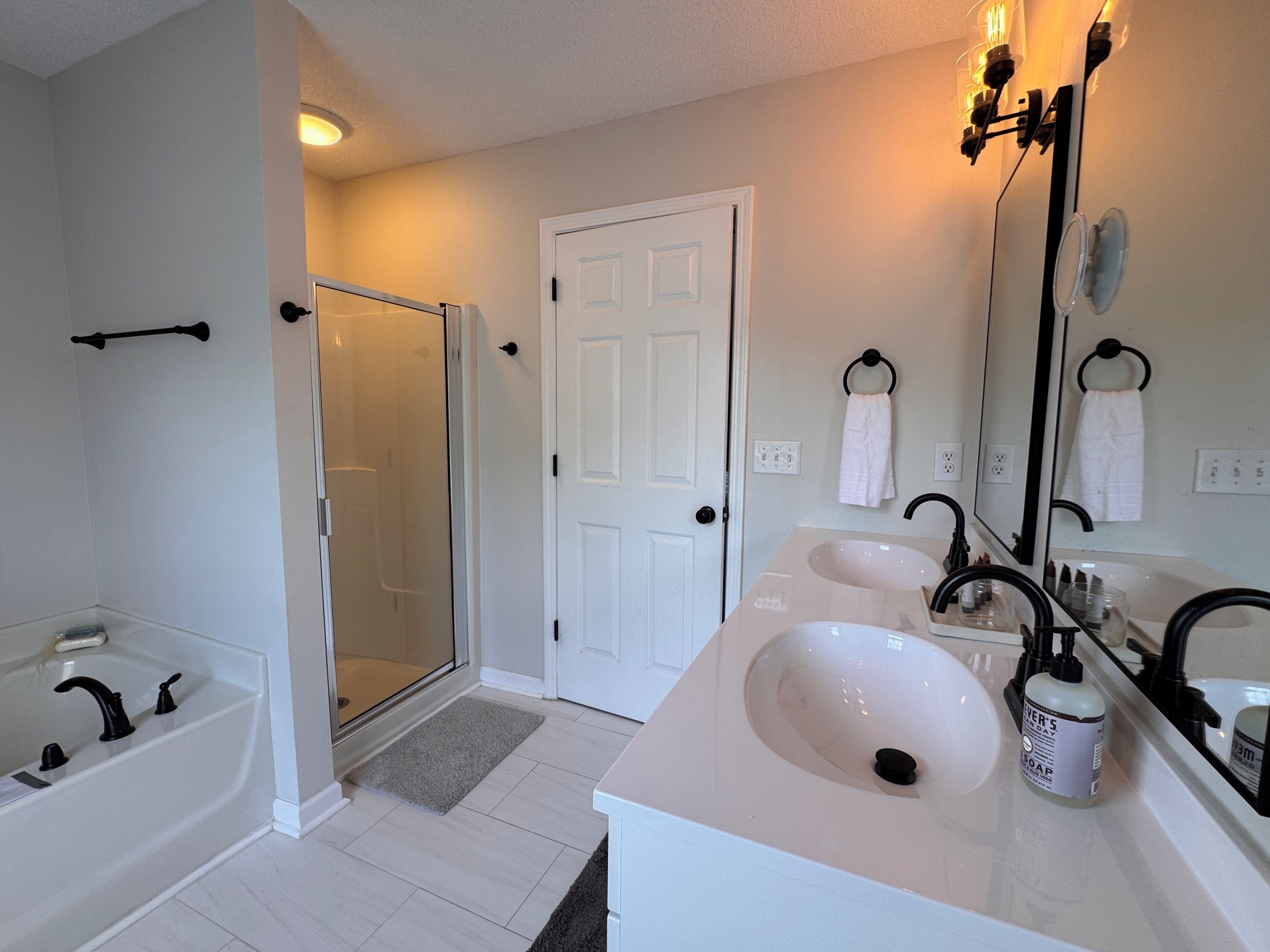 A bathroom with a bathtub, a shower, a double sink, and a large mirror.
