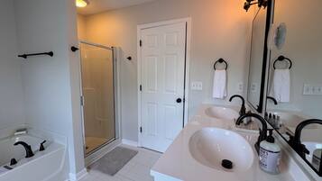 A bathroom with a bathtub, a shower, a double sink, and a large mirror.