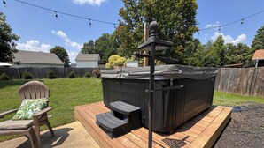 A hot tub on a wooden deck with a chair and a small table.