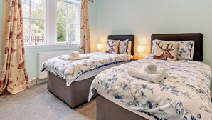 Une chambre avec deux lits, une literie à motifs floraux, une fenêtre avec des rideaux et un radiateur.