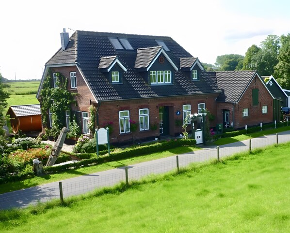 Une grande maison en briques, dotée de nombreuses fenêtres, d’un toit en pente et d’une cour clôturée.