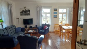 En opholdsstue med sofa, lænestole, et fjernsyn og et spiseområde med bord og stole.