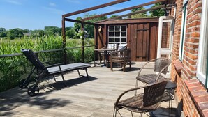 En træterrasse med udendørs møbler, en murstensmur og udsigt til et grønt område.