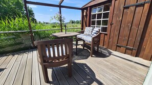 Une terrasse en bois avec une table et des chaises, une vue sur un champ verdoyant et un bâtiment en bois doté d’une fenêtre.