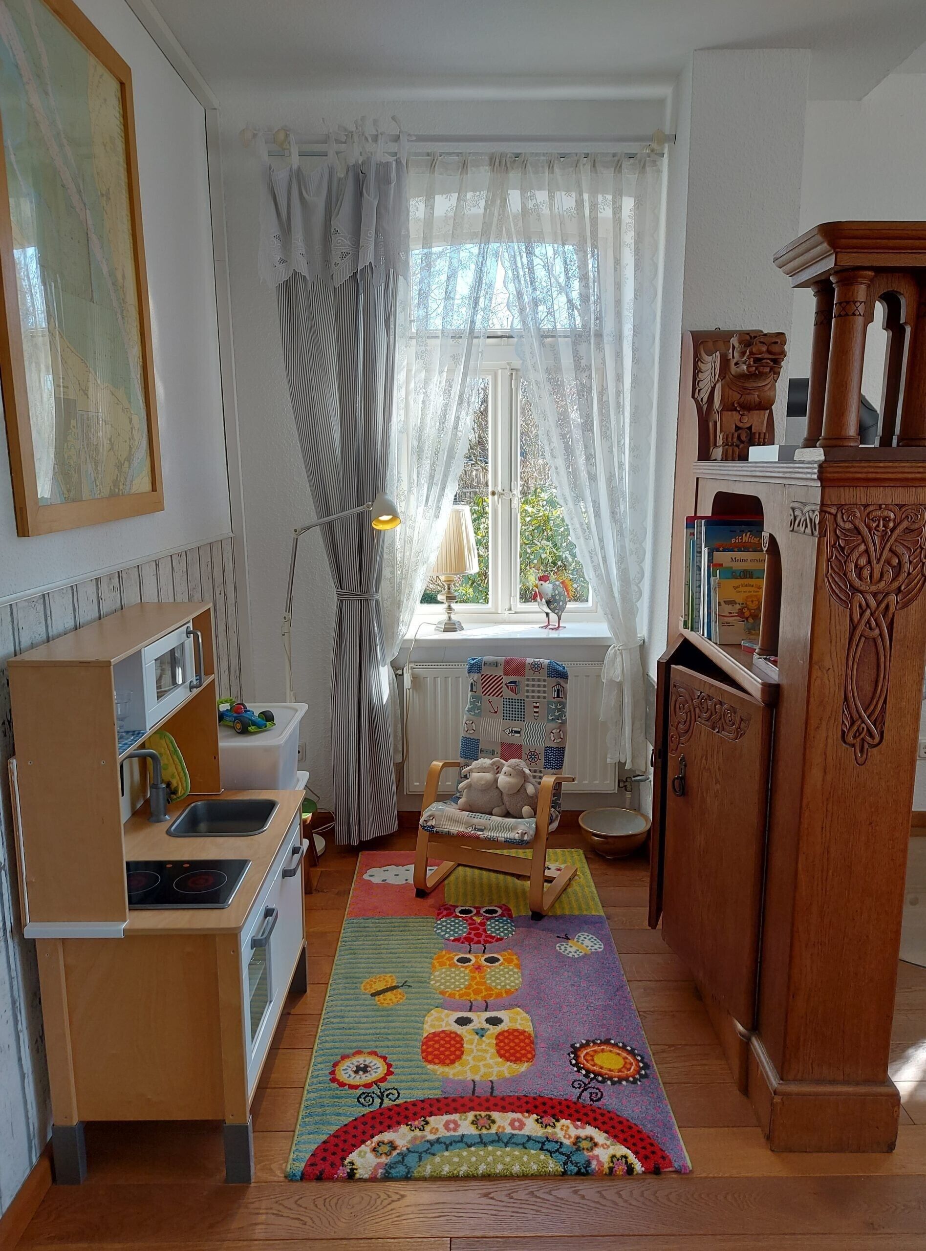 Ein gemütliches Zimmer mit Küchenzeile, einem fenster mit Vorhängen, einem Holzstuhl und einem Bücherregal.