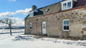 Ein Steinhaus mit geneigtem Dach, zwei Fenstern und einer Tür.