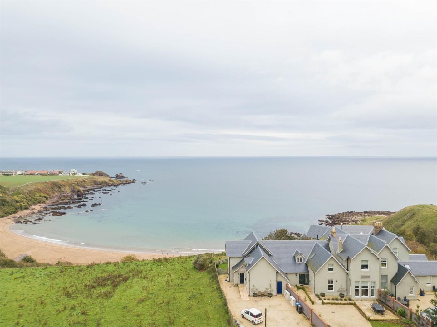Una propiedad costera con una casa grande, una playa de arena y vista al mar.