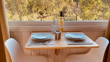 Una mesa de comedor con dos platos, una botella de vino y vasos, ubicada en un balcón con vista a árboles.
