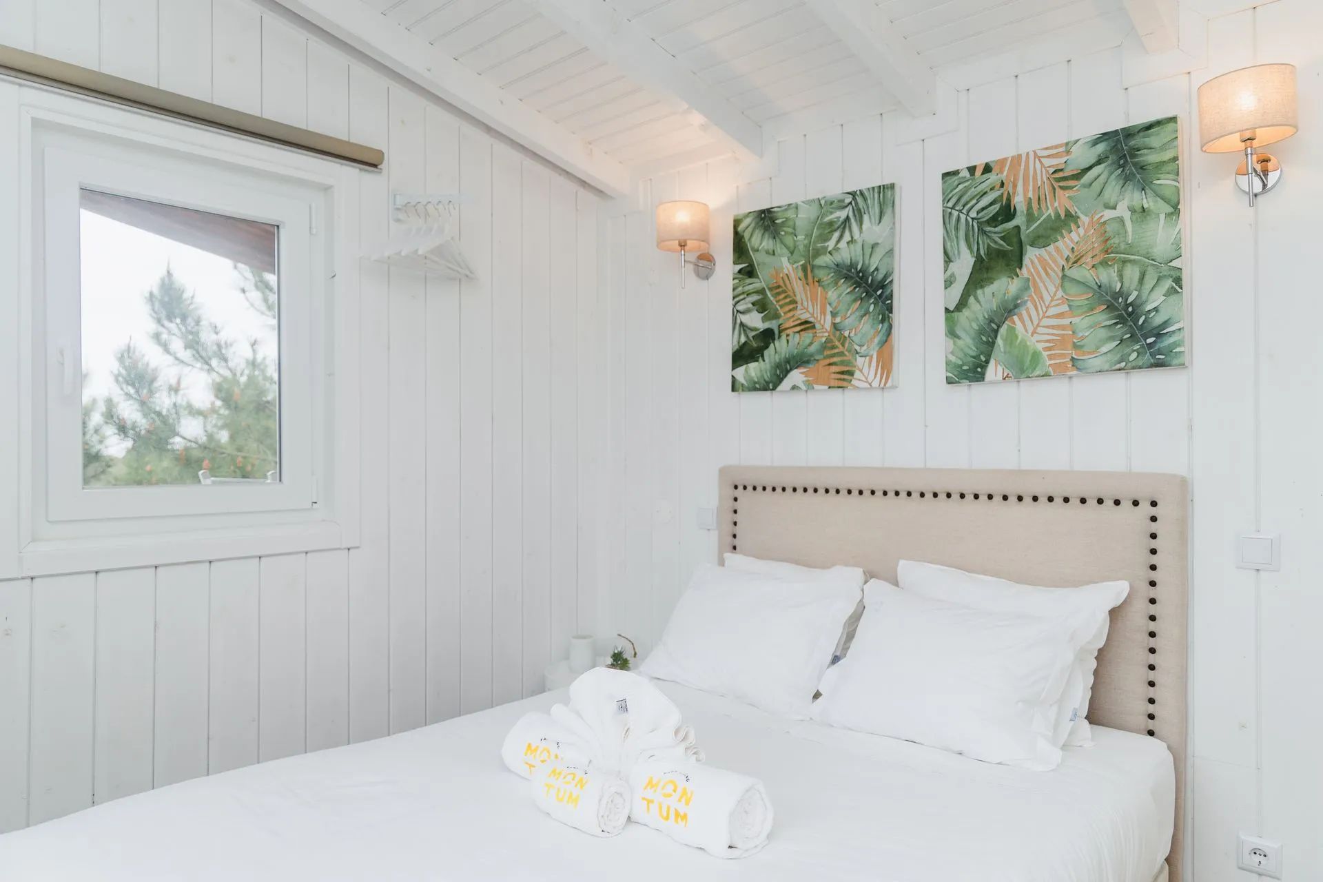 Ein Schlafzimmer mit einem Bett, weißen Wänden, einem Fenster und zwei Wandlampen.
