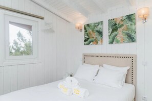 Un dormitorio con cama, paredes blancas, una ventana y dos lámparas de pared.