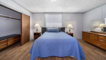 Une chambre à coucher comprenant un lit, des tables de chevet, une armoire, un miroir et une fenêtre avec des stores.