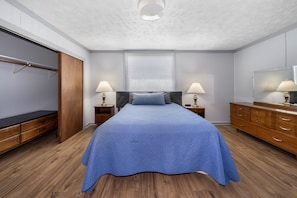 A bedroom with a bed, bedside tables, a wardrobe, a mirror, and a window with blinds. - Apartment in Beautiful Auburn Ne (Auburn)