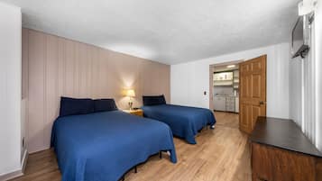 Un dormitorio con dos camas, un aparador de madera y una kitchenette al fondo.