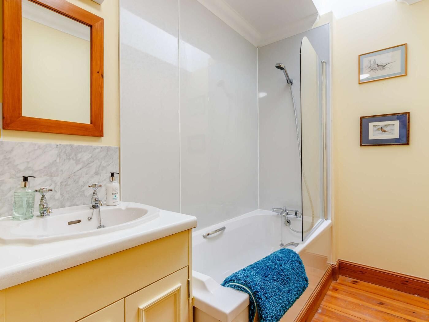 Un baño con bañera, ducha, lavamanos y dispensadores de jabón, y un espejo.