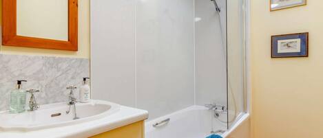 Un baño con bañera, ducha, lavamanos y dispensadores de jabón, y un espejo.