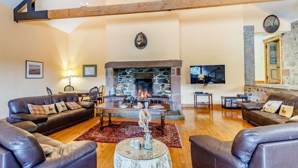 Ein gemütliches Wohnzimmer mit Kamin aus Stein, Ledersofas, einem Couchtisch und einem Fernseher.