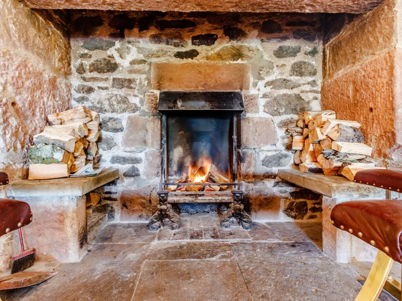 A stone fireplace with a fire, flanked by two wooden benches.
