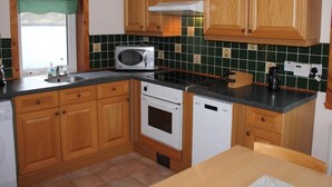 Uma cozinha com armários de madeira, micro-ondas, forno e máquina de lavar louça.