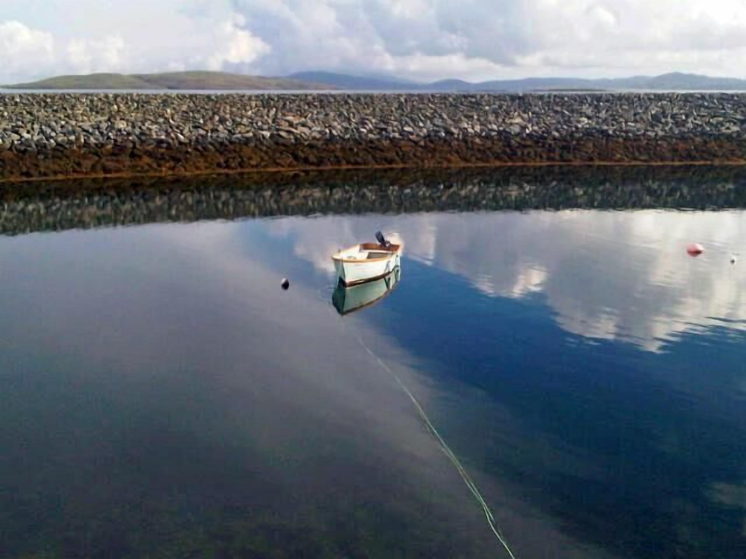 Une étendue d’eau calme où un bateau est amarré près d’une côte rocheuse.