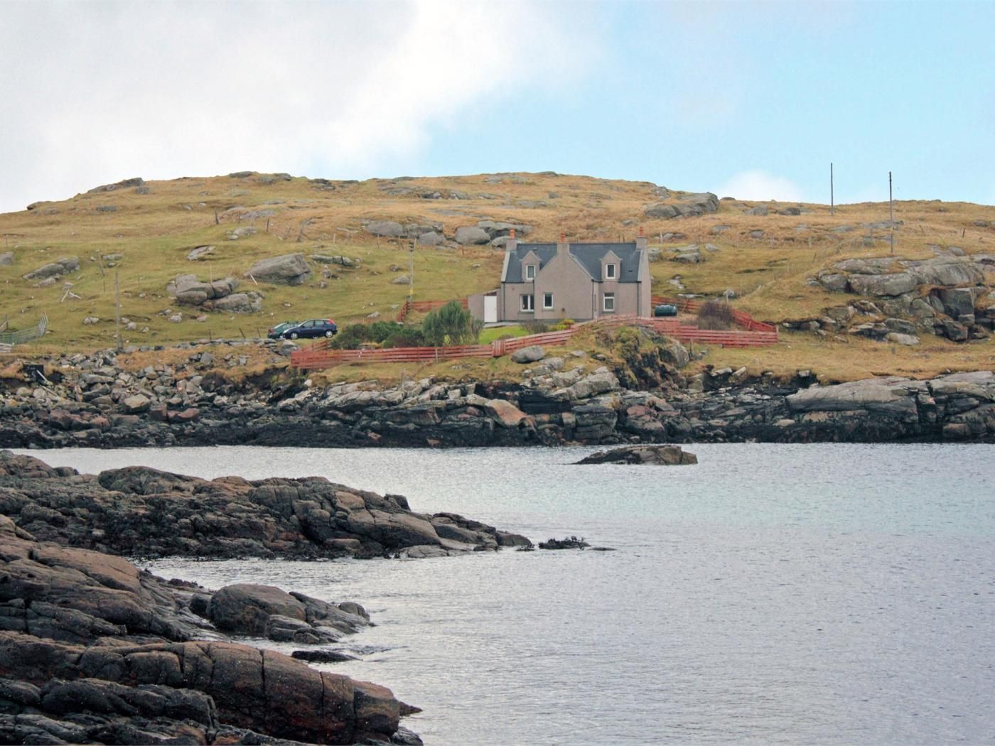 A coastal house with a stone foundation, a grey roof, and a fenced yard.