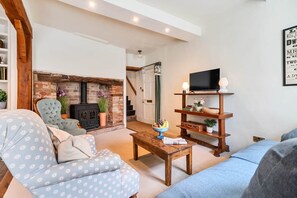 A cozy living room with a fireplace, a television on a wooden stand, and a staircase leading to another room. - Characterful Townhouse | Central 3 Bed + Parking (Ludlow)