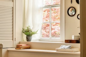A window with a view of autumn foliage, a potted plant, a stack of books, and a towel on a ledge.