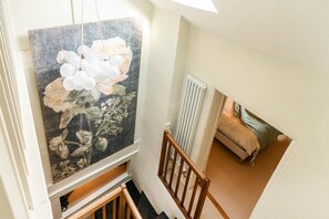 A high-ceiling room with a large floral painting, a radiator, and a bed with a striped blanket. - Characterful Townhouse | Central 3 Bed + Parking (Ludlow)