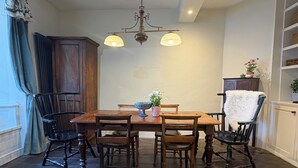Un comedor con una mesa de madera, cuatro sillas, una araña y un mueble con una planta.