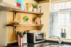A kitchen with a microwave, wooden shelves, a sink, and a window with curtains. - Characterful Townhouse | Central 3 Bed + Parking (Ludlow)