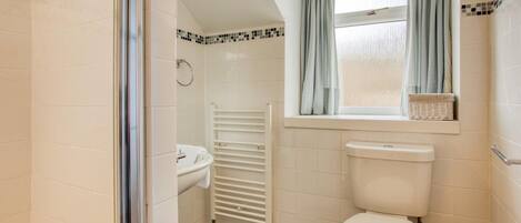 A bathroom with a white toilet, a white sink, a towel rack, a window with curtains, and a tiled floor.