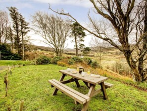 Une table de pique-nique est installée sur une pelouse, offrant une vue pittoresque sur les arbres et les collines en arrière-plan.