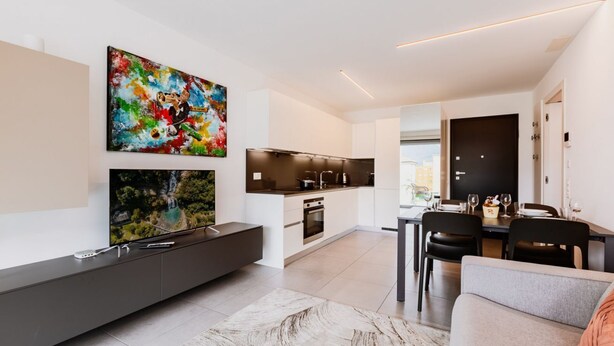 Una sala moderna con un televisor de pantalla plana, un comedor con mesa y sillas, y una cocina equipada con horno y microondas.