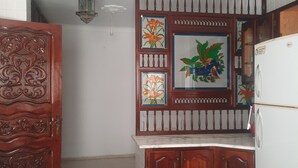 Cuina compacta amb nevera, un armari de fusta, una cadira i un panell decoratiu a la paret.