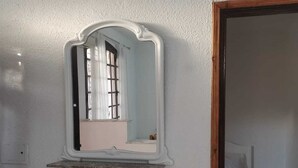 Una habitació amb un mirall a la paret, un llit i una porta que condueix a una altra habitació.