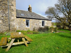 A stone building with two windows, a chimney, and a grassy yard with a picnic table. - 1 Bed in Isle Of Arran (oc-ca344) (Kilmory)