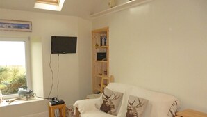 Une pièce confortable avec un canapé, un téléviseur fixé au mur, une petite table en bois et une fenêtre donnant sur un beau paysage.