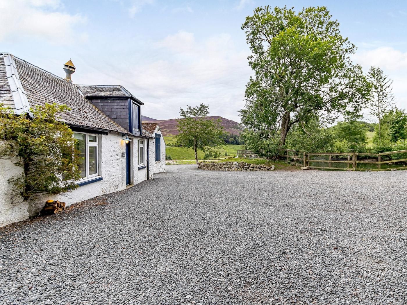 A white building with a gravel driveway, a stone wall, and a wooden fence.