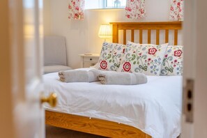 A neatly made bed with floral pillows and a folded towel, a bedside lamp, and a chair in a hotel room. - 1 Bed in Blairgowrie (oc-ca361) (Blacklunans)