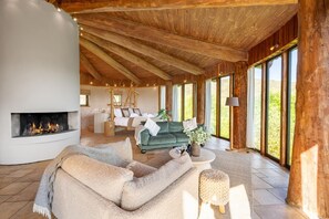 A spacious living area with a fireplace, a sofa, a coffee table, and a large window providing a view of the outdoors.